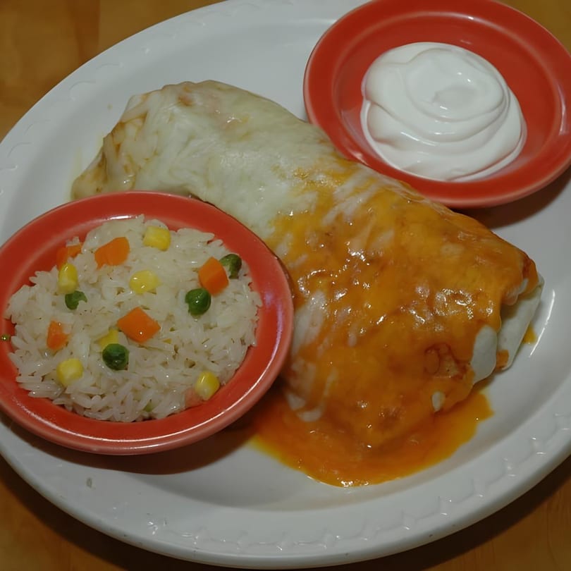 A Los Chorros Restaurant burrito covered in cheese sauce, with a side of rice and sour cream.