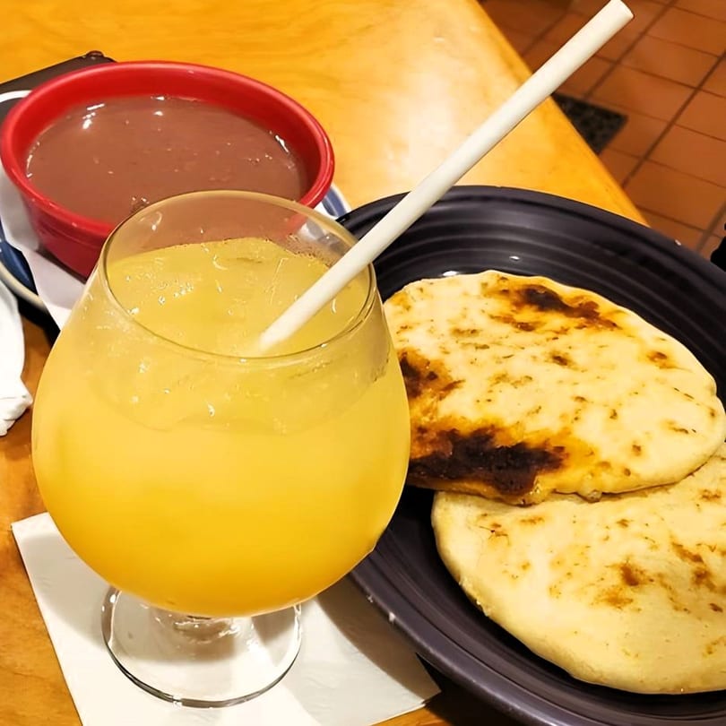 Pupusas and a glass of orange juice with a red bowl of beans on a wooden table.