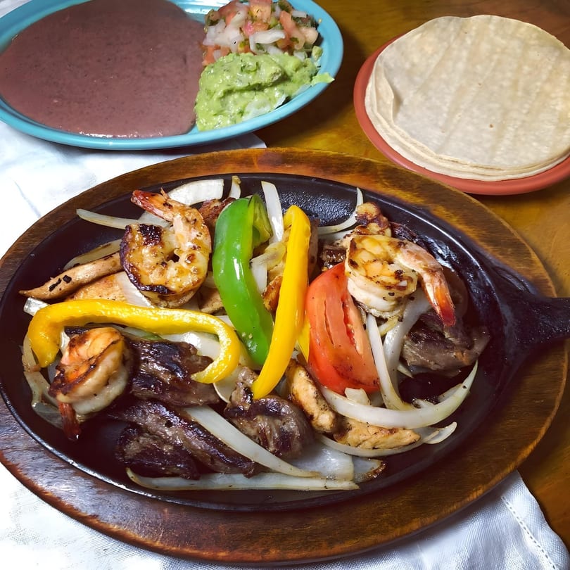 Sizzling fajitas with shrimp, steak, chicken, colorful peppers, and onions, served with sides.