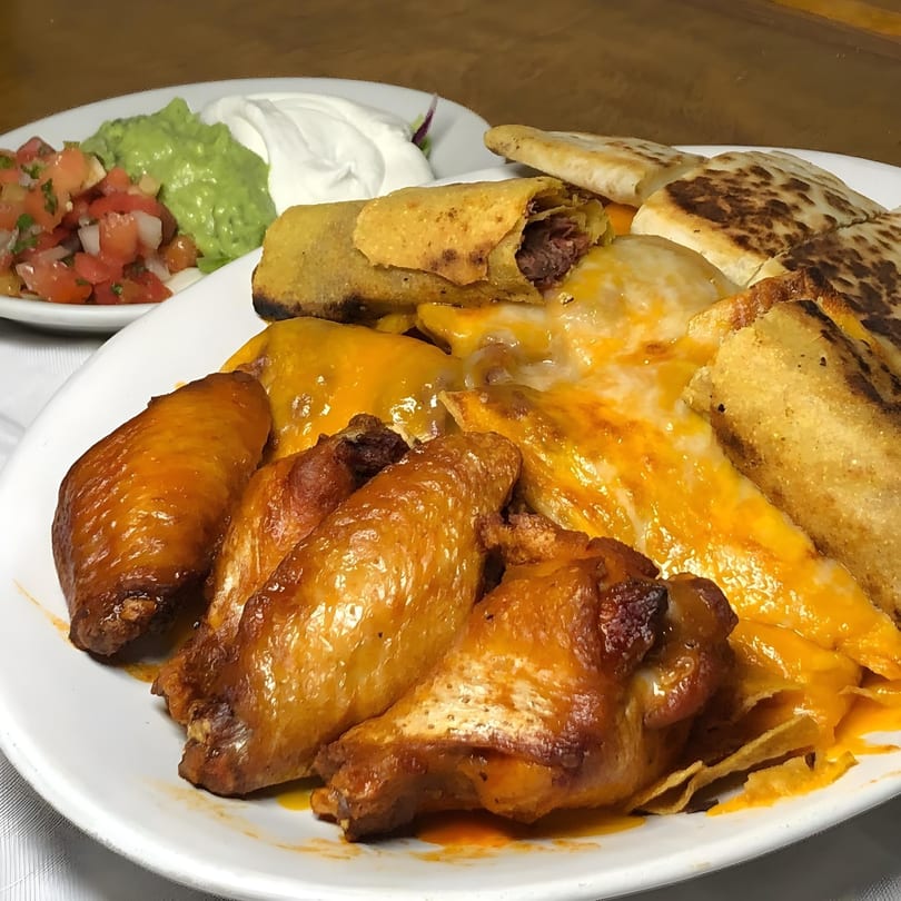 A large platter of Salvadoran food including chicken wings, taquitos, pupusas, and cheesy nachos.